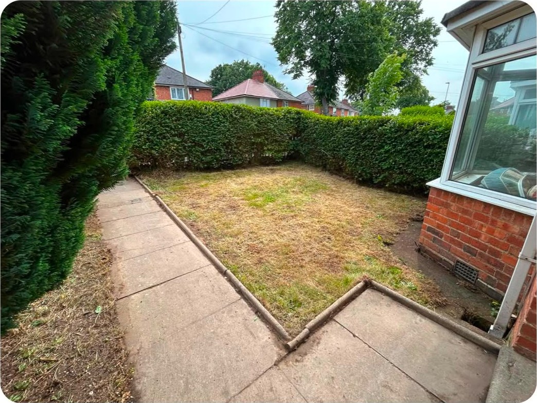 A back garden with a freshly cut lawn and neatly trimmed hedges beside a conservatory