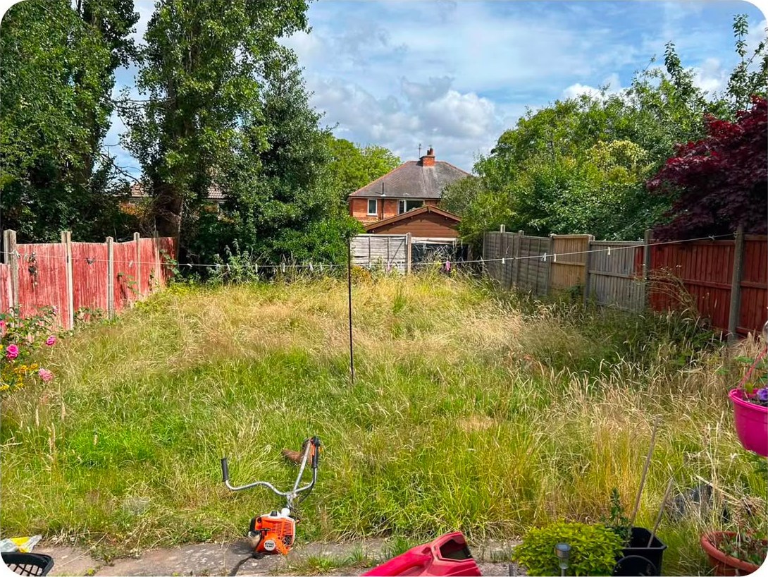 A strimmer standing ready at the edge of a long, overgrown lawn on a sunny day