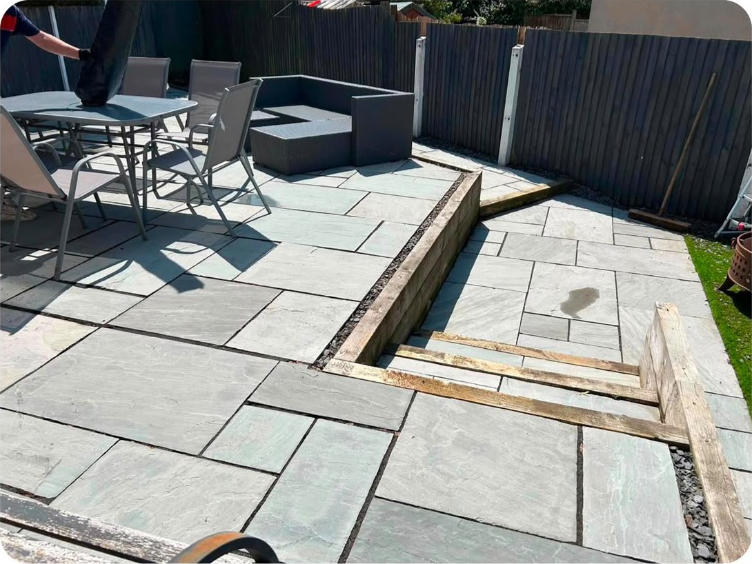 A slate patio with timber sleepers, offcuts and garden furniture left across it