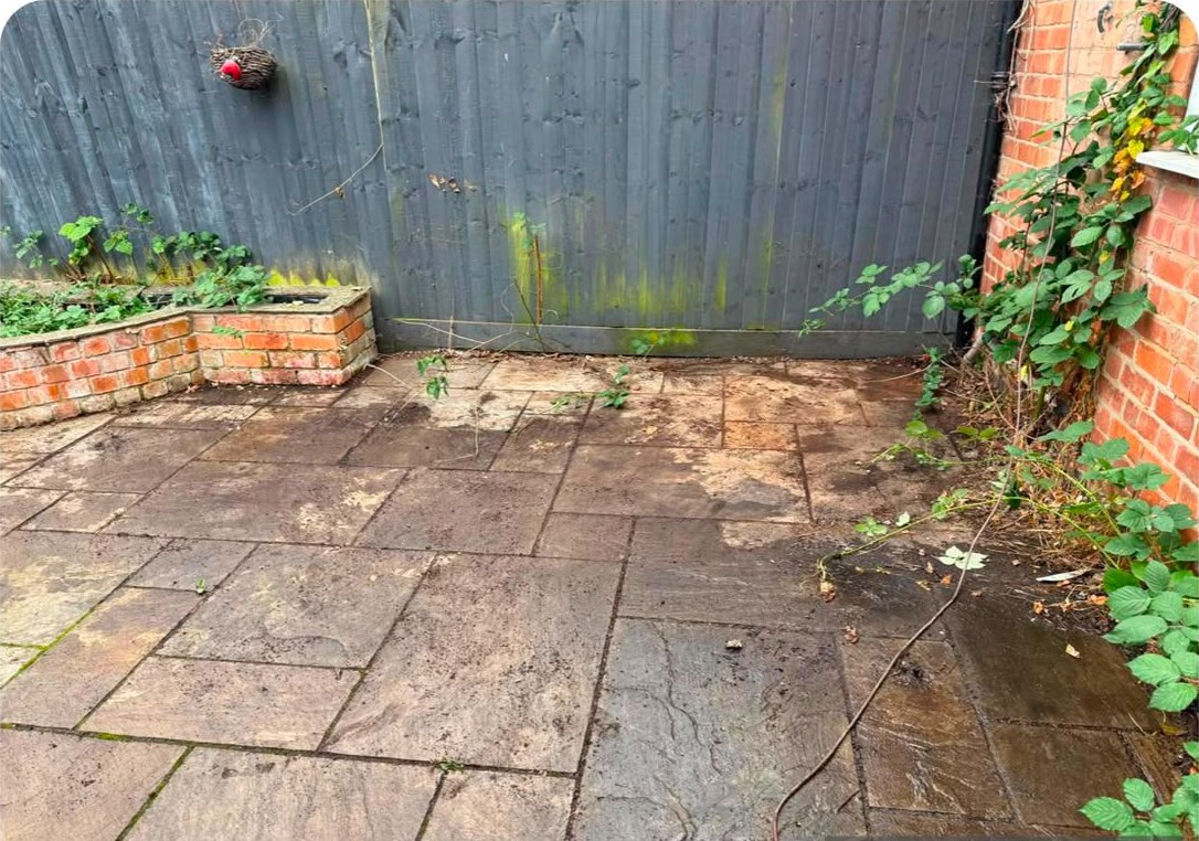 A paved yard cleared of rubbish, with a raised brick bed along the fence